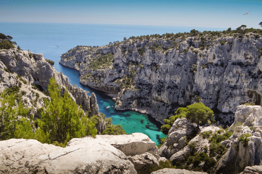 View of Calanque d’En-Vau with dramatic limestone cliffs and turquoise waters stretching to the sea, surrounded by pine trees and rugged rock formations. This breathtaking natural inlet near Cassis is one of the most popular day trips from Marseille for hiking, swimming, and scenic boat tours.
