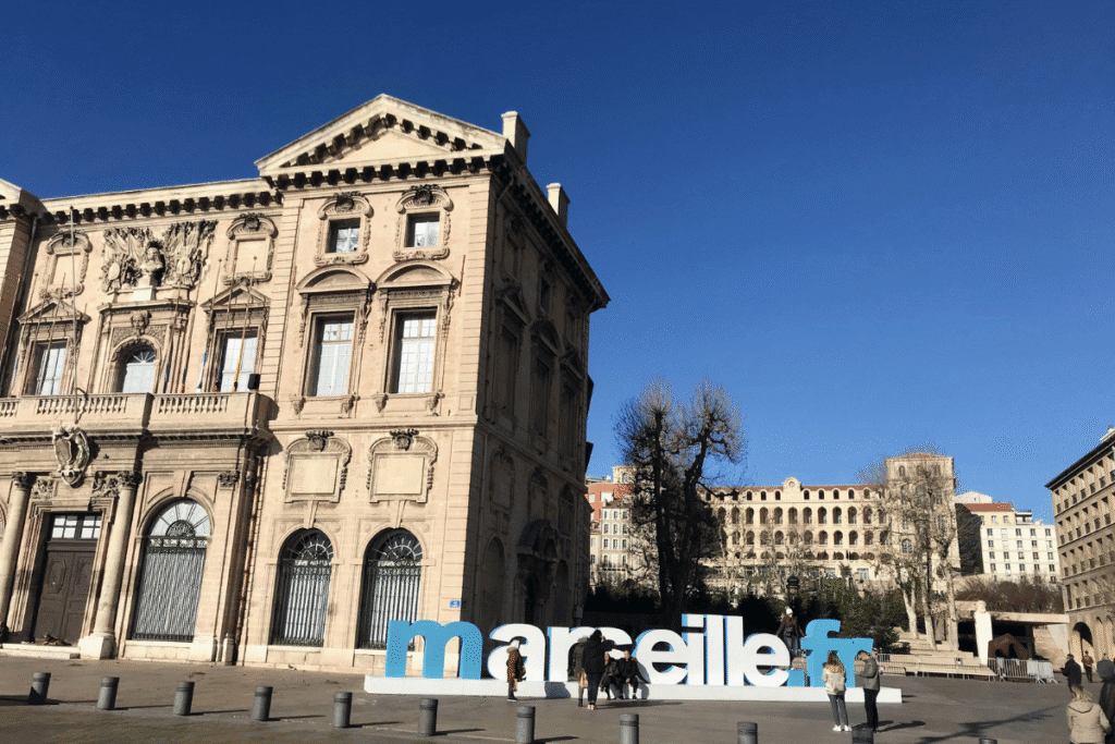 Tourists gathered around the large blue and white Marseille sign in front of the historic Hôtel de Ville building, a popular photo spot and starting point for any Marseille itinerary.