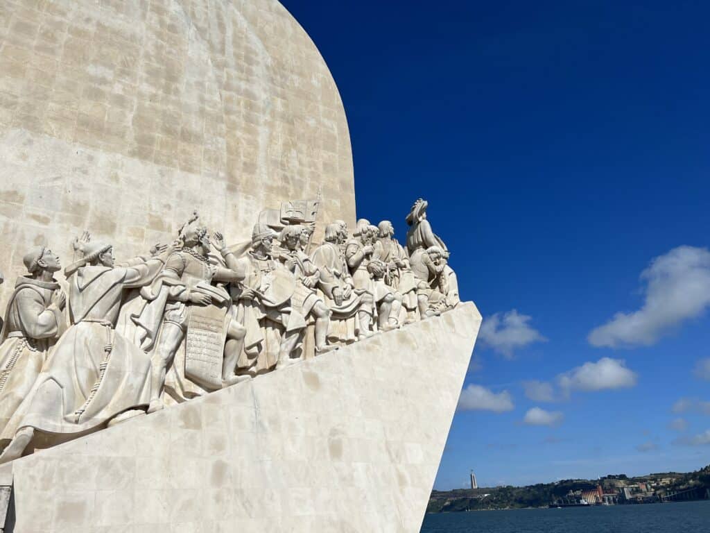 Monument of the Discoveries in Belém, Lisbon, featuring sculpted figures of Portuguese explorers facing the Tagus River under a clear blue sky, a striking historical stop on a Lisbon itinerary.