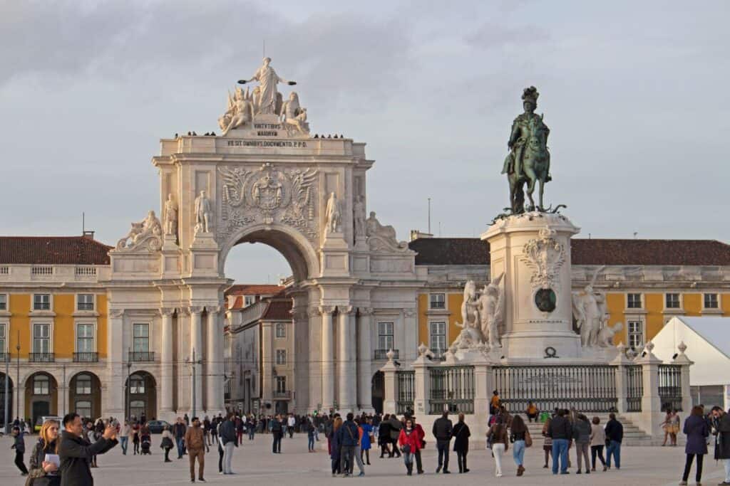 People gather in Lisbon’s Praça do Comércio with the Arco da Rua Augusta and equestrian statue in the background under soft daylight. The lively square captures the historic charm and atmosphere that makes Lisbon worth visiting.