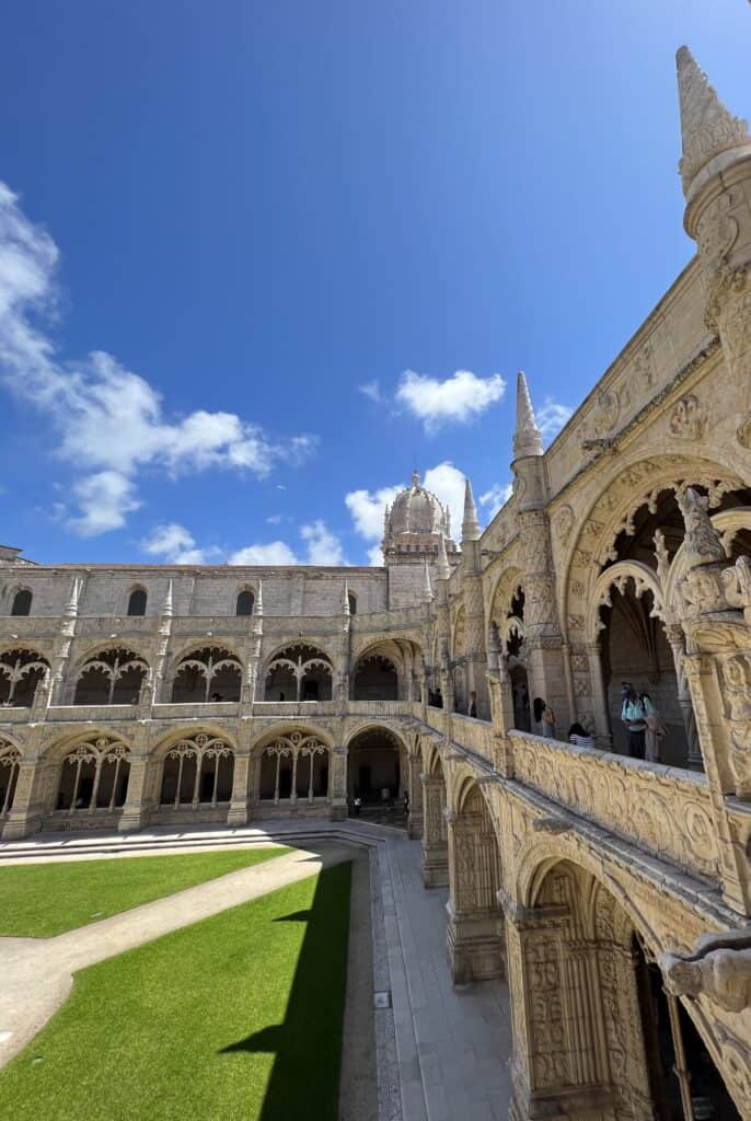 Cloister courtyard of Jeronimos Monastery features intricate stone arches, columns, and detailed carvings surrounding a green lawn. The UNESCO site is a highlight of Lisbon’s history and fits perfectly into a 3 day itinerary Lisbon.
