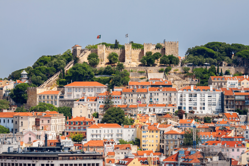 Lisbon skyline shows Castelo de Sao Jorge rising above red rooftops and pastel buildings on a sunny day. The hilltop castle is a key landmark to explore on a 3 day itinerary Lisbon.