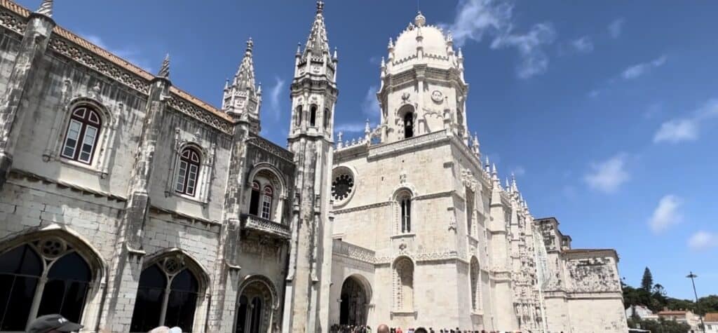 The grand limestone facade of Jerónimos Monastery, a UNESCO World Heritage Site, rises under a bright blue sky in Belém district Lisbon. Ornate towers arches and carved details show the elaborate Manueline architecture Lisbon is famous for.
