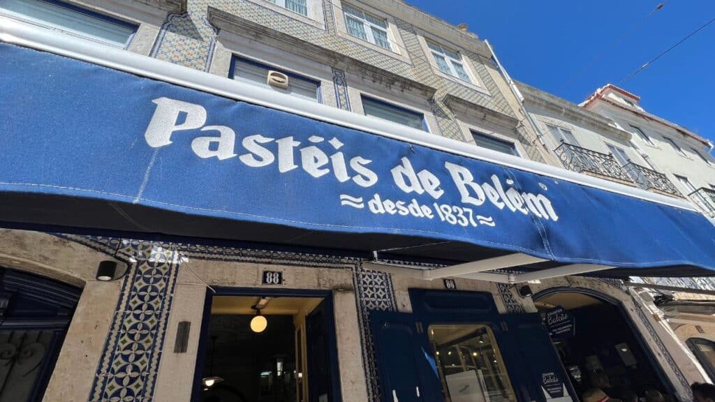Blue awning above the famous bakery entrance in Belém district Lisbon with the words "Pasteis de Belem desde 1837". The historic shop is known for serving the iconic pastel de nata Lisbon visitors line up to taste.