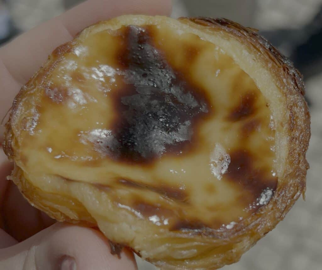 Close view of a freshly baked pastel de nata Lisbon held in a hand with glossy custard and caramelized top inside a flaky pastry shell. The famous Portuguese dessert is popular in the Belém district Lisbon.