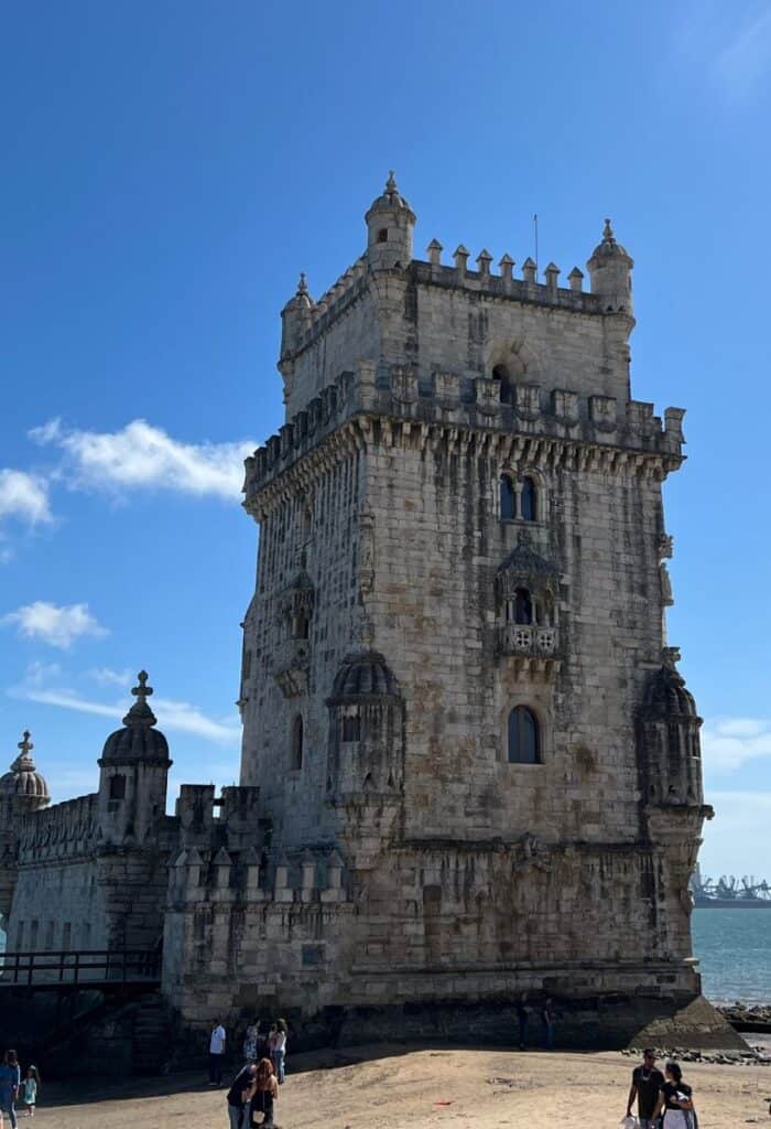 Belém Tower Lisbon UNESCO site rising above the waterfront along the Tagus River in Belém district Lisbon. Visitors stand near the base of the historic fortress built in ornate Manueline architecture.
