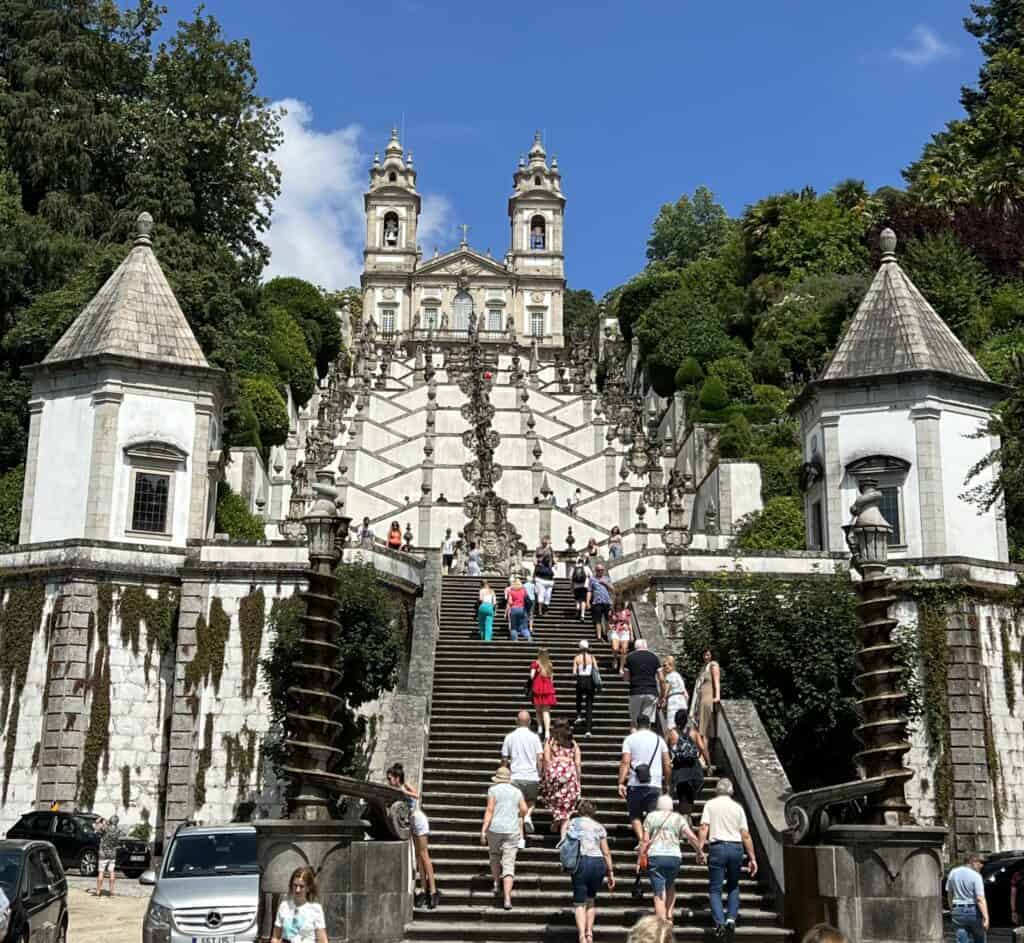 Visitors climb the grand staircase of Bom Jesus do Monte with ornate fountains and a church at the top surrounded by greenery. This iconic day trip is a memorable addition when planning how to spend 3-5 days in Porto.