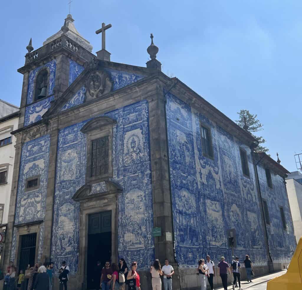 Chapel of Souls in Porto covered in blue and white azulejo tiles depicting detailed historical scenes with visitors gathered outside. Seeing these iconic tiled buildings is a must when deciding how many days in Porto.