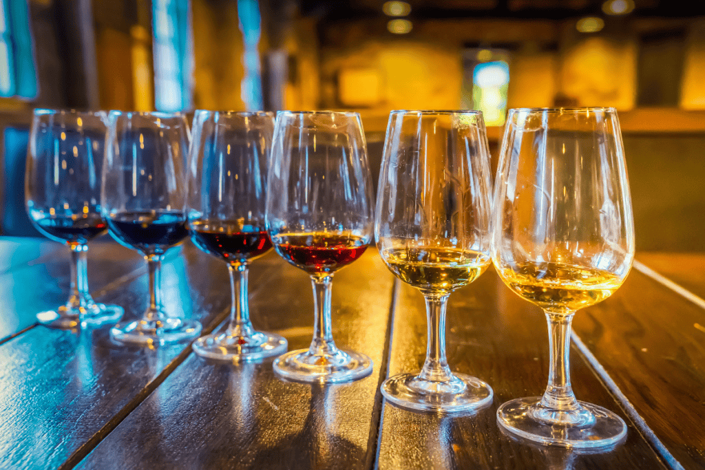 A row of wine glasses filled with red and white port sits on a wooden table in a warmly lit tasting room. Sampling port wine is one of the most popular things to do in Porto.