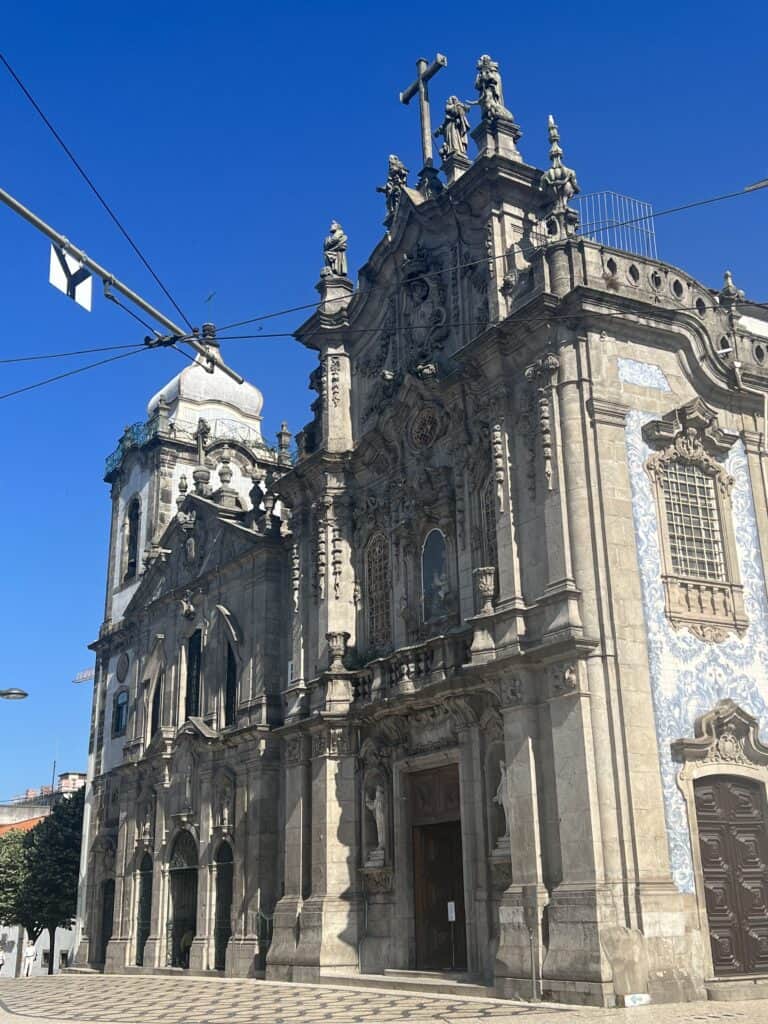 The twin churces in Porto covered in blue and white azulejo tiles depicting detailed historical scenes with visitors gathered outside. Seeing these iconic tiled buildings is a must when deciding how many days in Porto.
