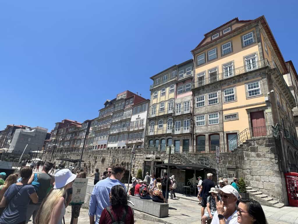 Colorful historic buildings rise above the busy Ribeira waterfront in Porto. Crowds gather near the riverfront stairs in the heart of the Porto UNESCO World Heritage Site.