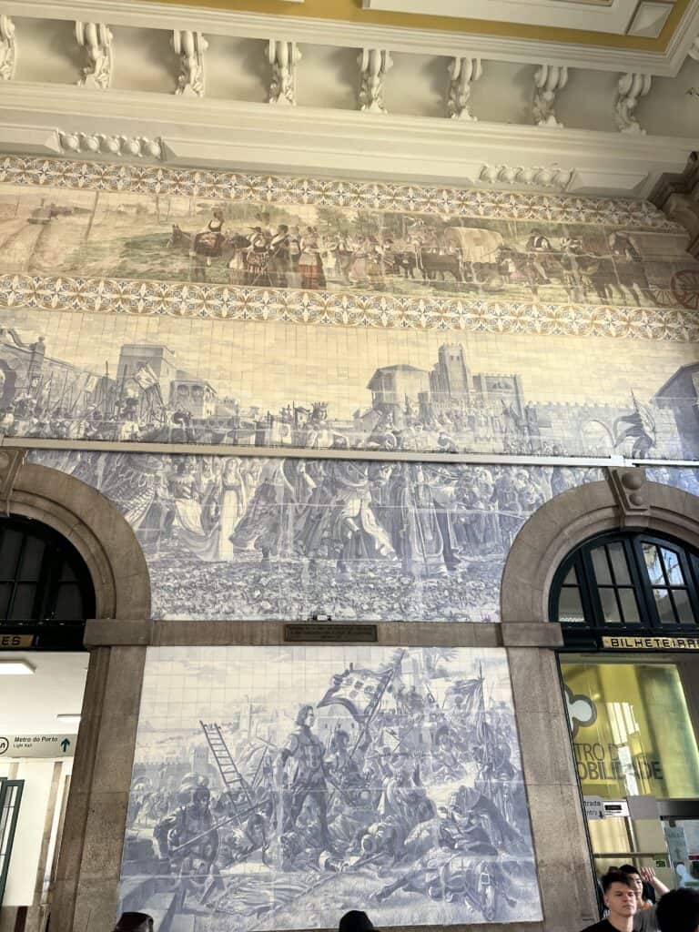 lue and white azulejo tile murals cover the walls inside São Bento Railway Station in Porto. The scenes show processions and daily life.
