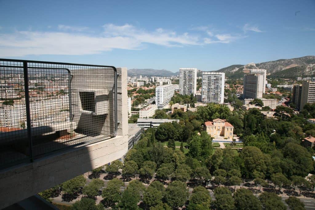 View of the city of Marseille from Cité Radieuse, including the top of trees, tall buildings, and hills in the background.