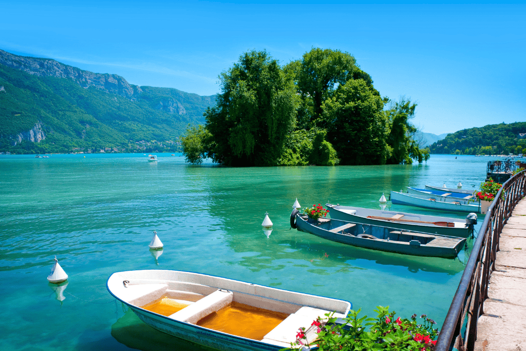 Clear blue waters of Lake Annecy with boats that can be rented and the French Alps in the background.